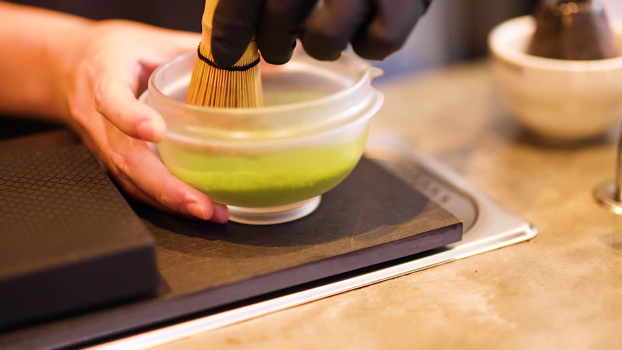 Hands whisking matcha in a bowl on a countertop, highlighting traditional tea-making techniques with warm lighting