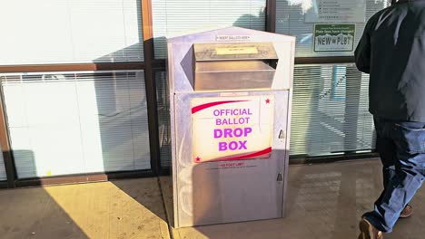 man votes in election by casting ballot in mail-in letter slot at official ballot drop box sign for american democratic government presidential race