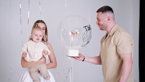 man holding a cake standing near his wife with baby in hands. little kid tries to reach the dessert. family celebration. studio footage.