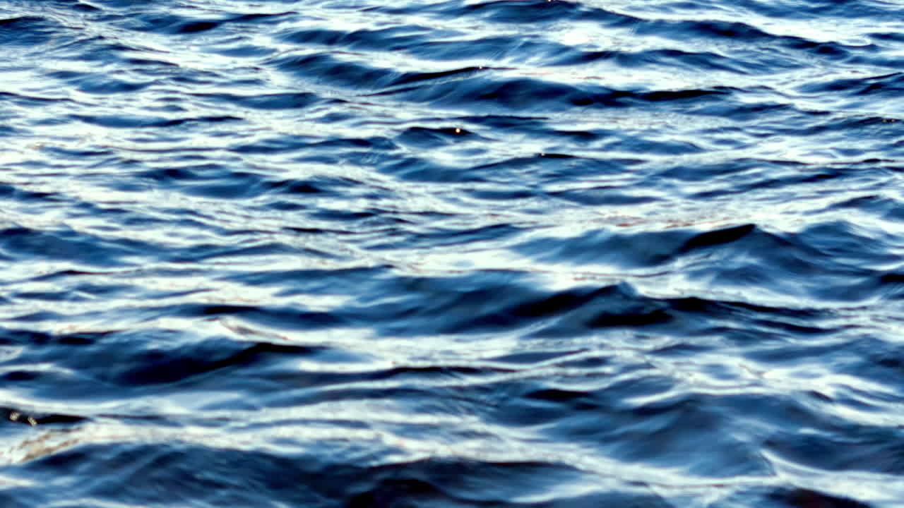 Close-Up View of Deep Blue Water with Gentle Ripples and Subtle Sunlight Reflections, Creating a Textured Surface Indicative of a Calm Ocean or Large Lake on a Bright Day