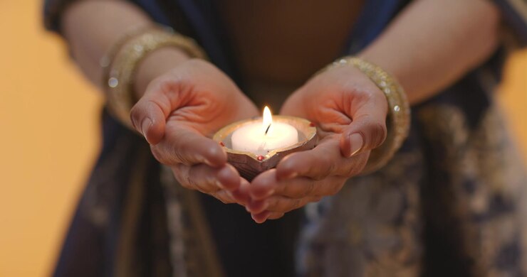 Ritual is starting, hands are cupping lit earthen diya and steadying flame for offering