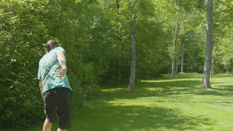 a man releases a disc during a disc golf throw in a wooded area, showcasing the sport's integration with nature