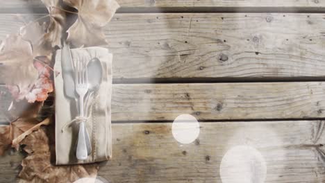 animation of light spots over cutlery and leaves on wooden background