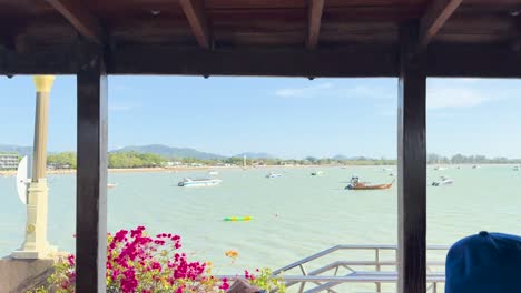 a tranquil ocean scene with boats and flowers under a wooden canopy in chalong bay, phuket. bright daylight enhances the vibrant colors