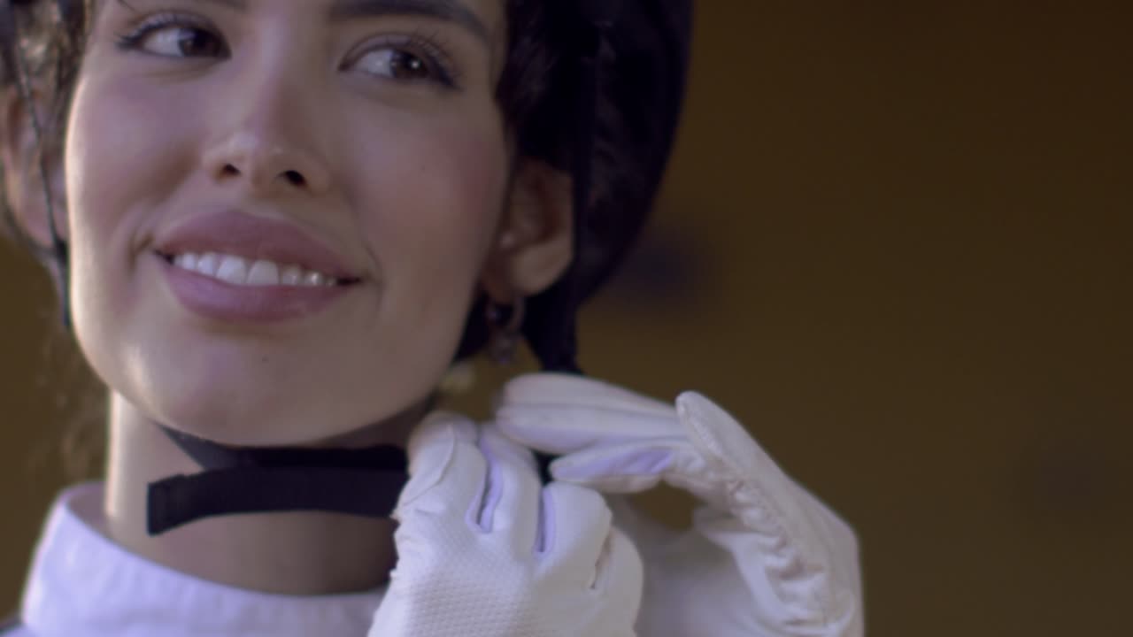 una hermosa mujer ecuestre es capturada en cámara lenta mientras aprieta la correa de su casco, sonriendo en previsión de su paseo