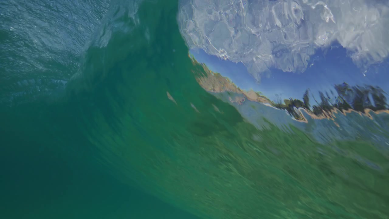 Un'onda che si infrange passa sopra la testa attraverso l'acqua limpida e turchese dell'oceano con la sua superficie curva sottostante, vista media da dietro di un'onda a tunnel.