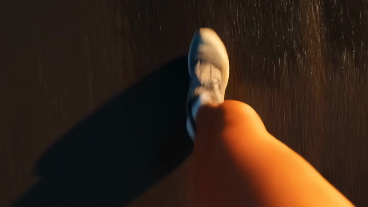Punto di vista dall'alto mostra il piede destro a metà passo con una sneaker bianca e un calzino alla caviglia basso su asfalto scuro, con la gamba di un pantalone arancione che riempie il primo piano e un forte contrasto notturno, con sneaker, scarpa, piede