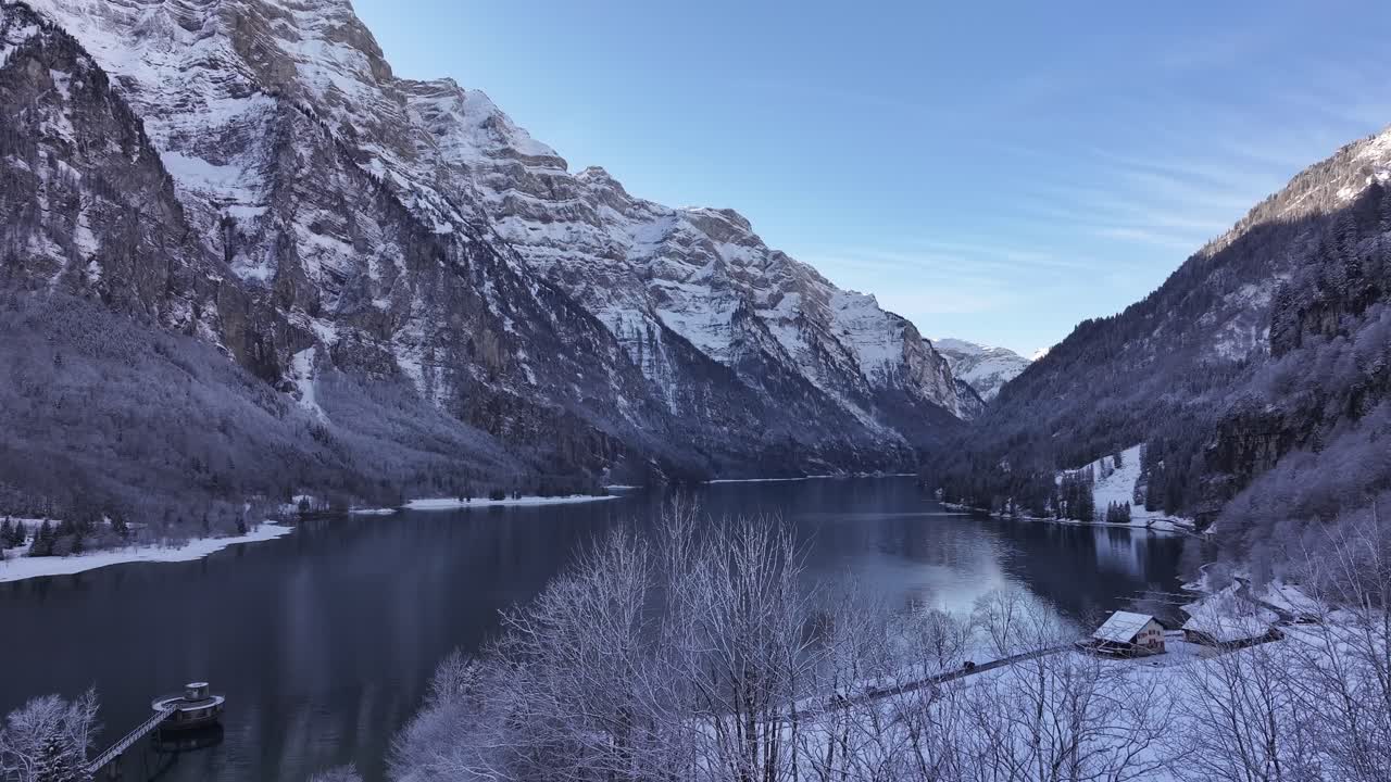 Henkeäsalpaava ilmakuva Klöntalersee-järvestä talvipäivänä, esitellen sen seesteistä kauneutta ja ympäröivää lumista maisemaa