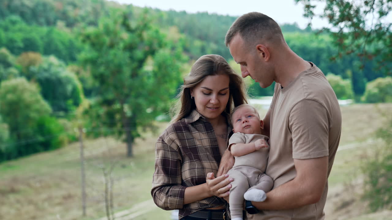 Caucasian couple with their infant baby standing outdoors. Mom and dad protecting their son from the wind. Mother kisses the baby on the head.