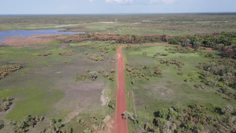 Toma-Aérea-De-Drones-De-Movimiento-Lento-Y-Alto-De-Una-Larga-Y-Recta-Carretera-Roja-Y-Matorrales-Verdes-Cerca-Del-Parque-Natural-De-La-Selva-De-Holmes,-Darwin,-Territorio-Del-Norte