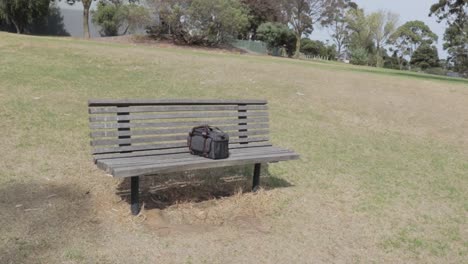 Pequeño-Bolso-De-Cámara-Azul-Grisáceo-Dejado-En-Medio-De-Un-Banco-De-Parque-De-Madera