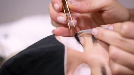 esteticista de cultivos con pinzas aplicando pestañas artificiales en el cliente