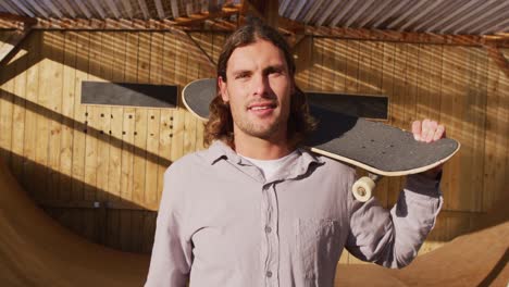 video de un feliz skateboarder caucásico sosteniendo un skateboard en un parque de skate