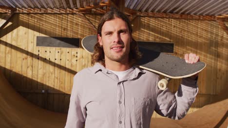 video of happy caucasian male skateboarder holding skateboard in skate park