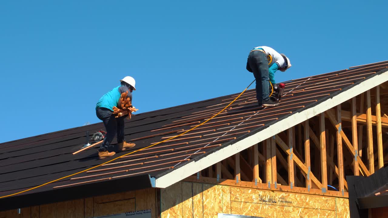 dos trabajadores clavando listones de madera para la instalación de tejas de cerámica en un edificio residencial usando una pistola de clavos de aire - nueva construcción de techos en california rodada en 4k