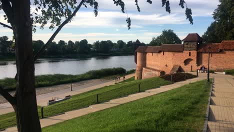 Frente-Al-Río-Nogat-En-Malbork,-Polonia-En-La-Hermosa-Puesta-De-Sol-Con-Un-Castillo,-Las-Paredes-De-Ladrillo-Rojo-Y-Gente-Irreconocible