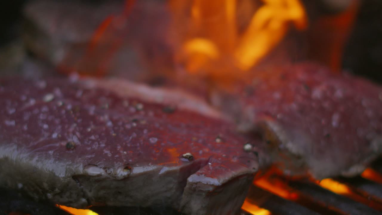 filetes de filete sazonados cocinados en una parrilla de barbacoa con llamas cocinando carne con pimienta cayendo en cámara lenta