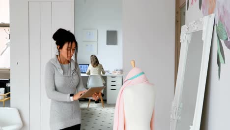 fashion designer using tablet and examining the fabric on dressmakers model 4k