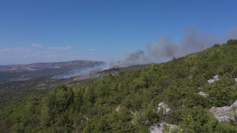 Volando-Sobre-Un-Bosque-Verde-Con-Humo-Saliendo-De-Un-Incendio-Forestal-En-La-Distancia