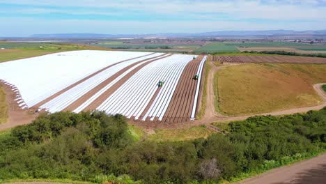 antena de tractores colocando filas de cubiertas de plástico en campos agrícolas cerca de santa maría california