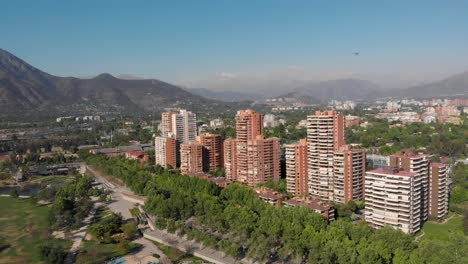 revelación aérea de edificios de apartamentos de lujo mientras un helicóptero cruza el horizonte en el parque bicentenario, santiago de chile, 4k