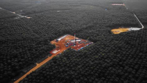 cinematic 4k drone footage of onshore drilling rig equipment structure for oil exploration and exploitation in the middle of jungle surrounded by palm oil trees during sunset and high oil price