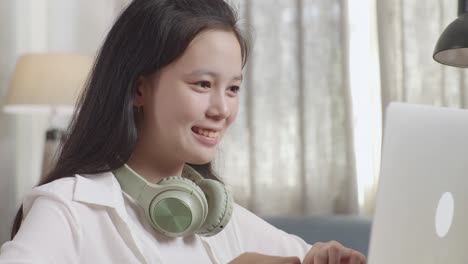 teenage girl smiling and giving a thumbs up while using a laptop