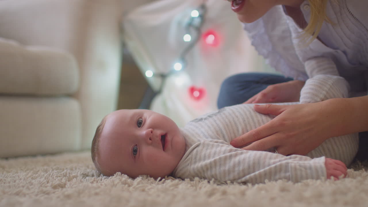 Loving mother playing game and tickling baby son lying on rug in child's bedroom at home - shot in slow motion