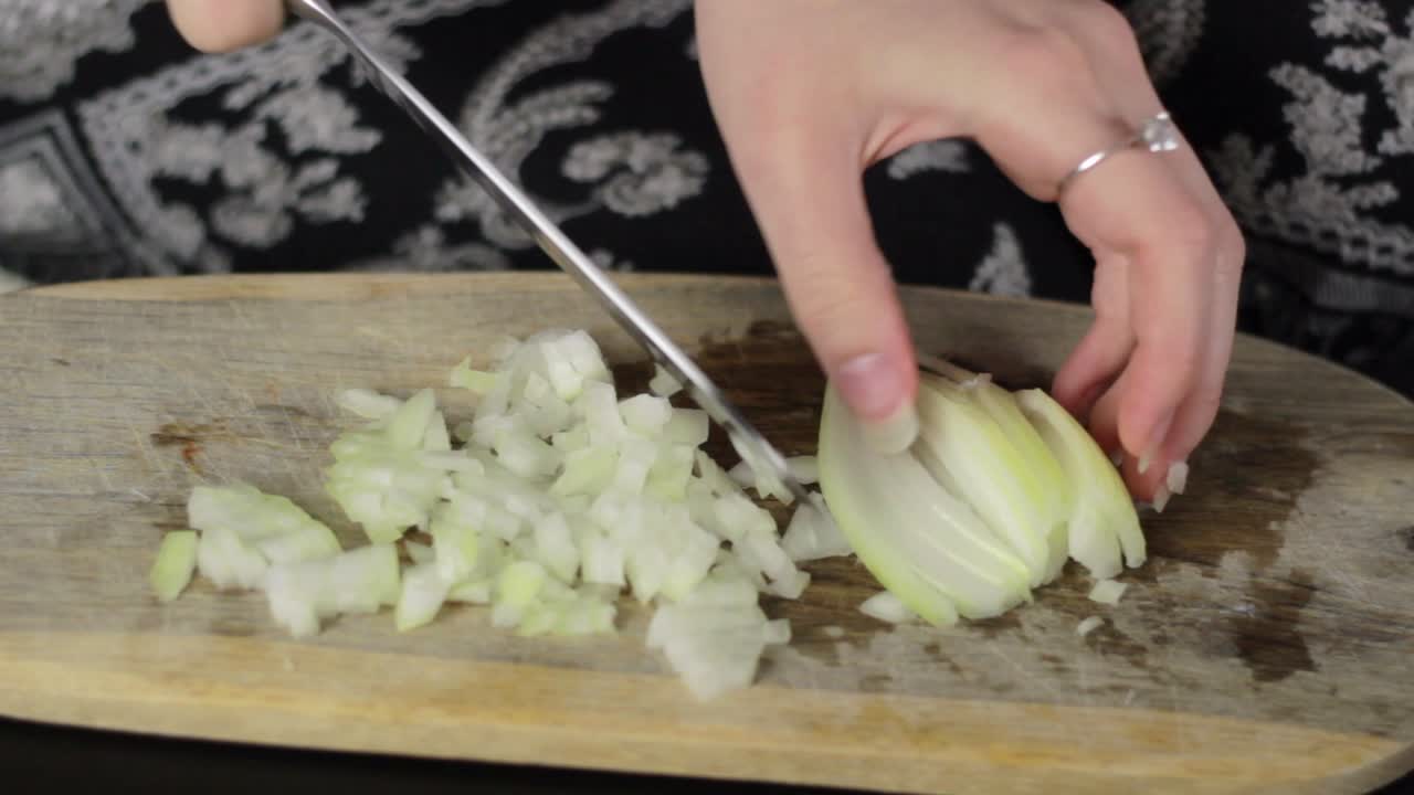 Woman use a kitchen knife to chop the onions on a cutting board, close up