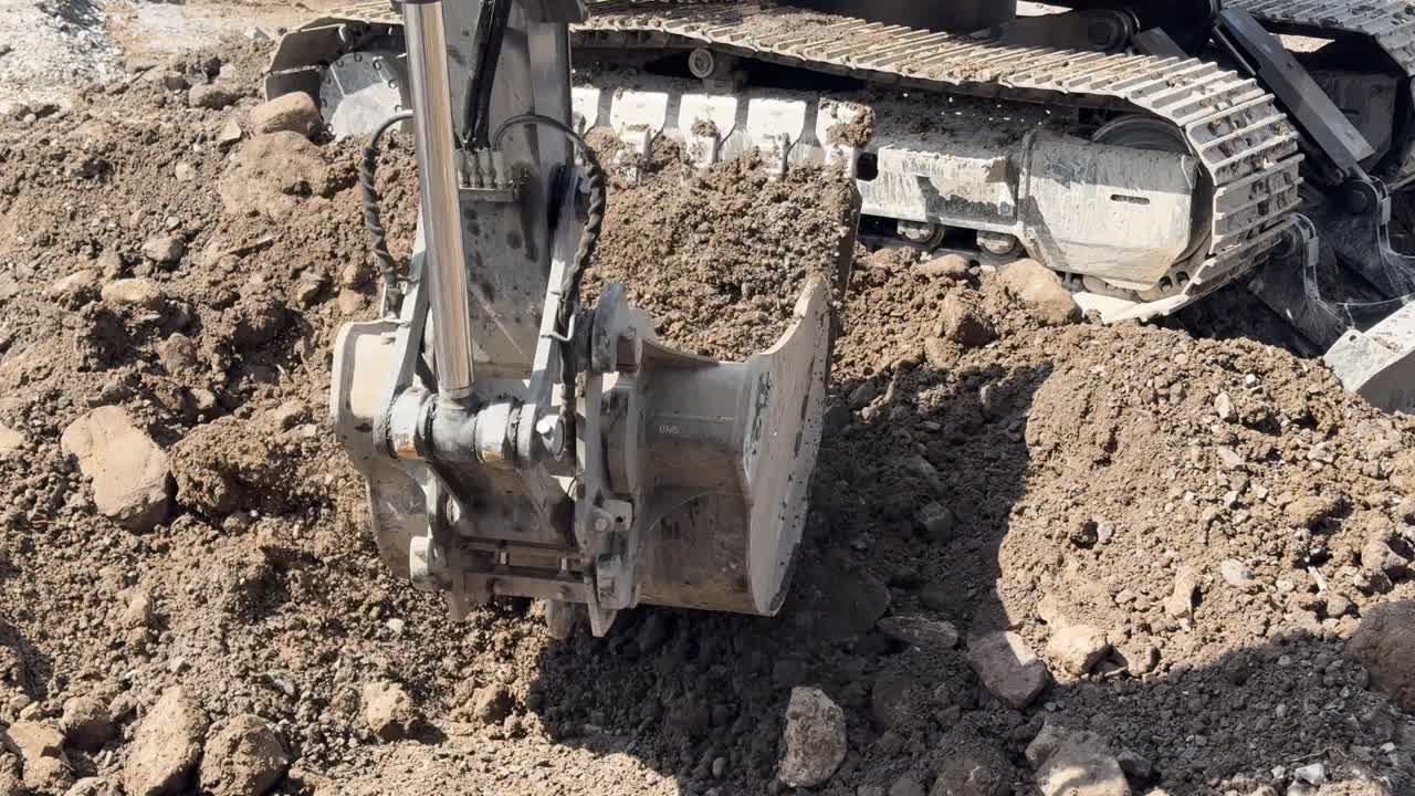Front loader tractor scoops dirt and rocks on construction site, lifting and dumping off-camera into dump truck.