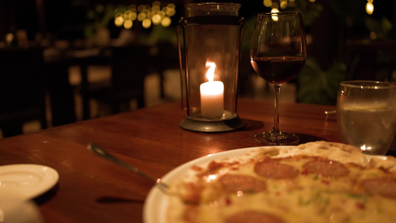 Primo piano di una pizza ai peperoni su un tavolo di legno illuminata da una calda luce di candela di notte