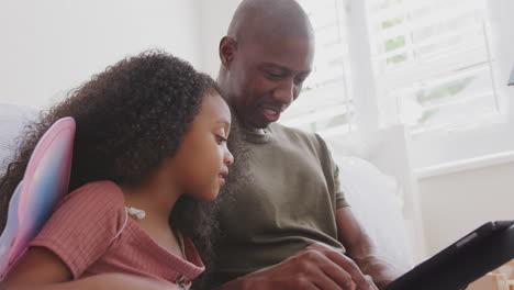 Padre-Con-Hija-Sentada-En-El-Suelo-En-El-Dormitorio-Del-Niño-Usando-Una-Tableta-Digital-Juntos