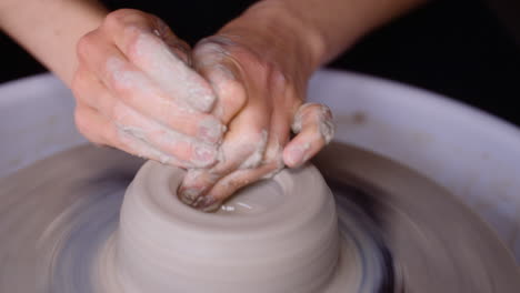 potter shapes clay on her pottery wheel with wet hands