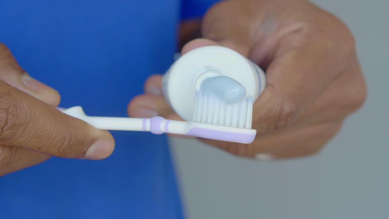 A man's hands squeezing toothpaste onto a toothbrush.