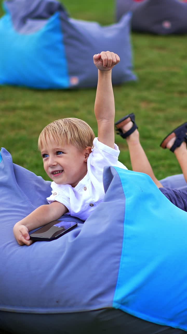 Cute cheerfull kid outdoor playing with phone. Little happy child having fun with smartphone. Vertical video