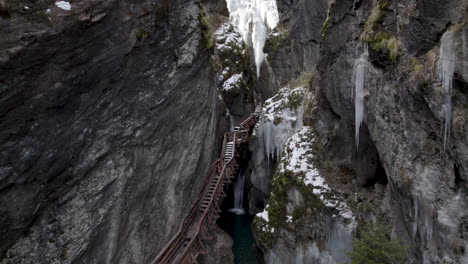 drone volando hacia atrás entre dos acantilados con un pequeño río con hielos en las paredes y una escalera subiendo en austria en el sigmund thun klamm