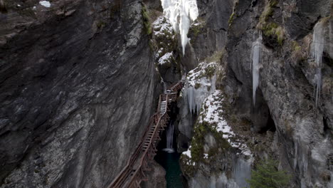 drone flying backwards between two cliffs with a small river with icicles on the walls and a staircase going up in austria at the sigmund thun klamm