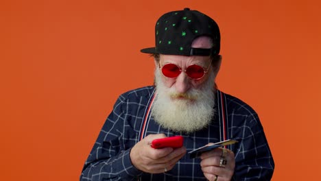 Senior-old-stylish-bearded-man-using-credit-bank-card-and-smartphone-purchases-online-shopping