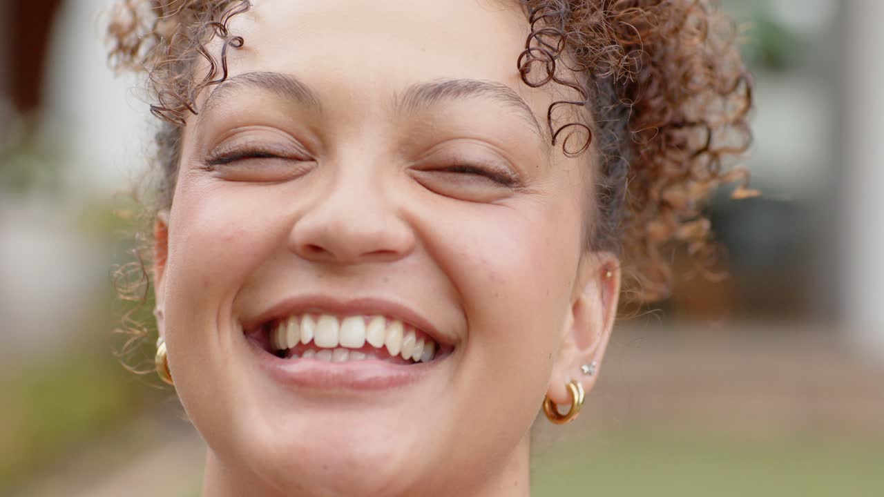 Mulher afro-americana passando da calma para o riso, inclinando a cabeça perto da varanda, exibindo brincos de argola de ouro.