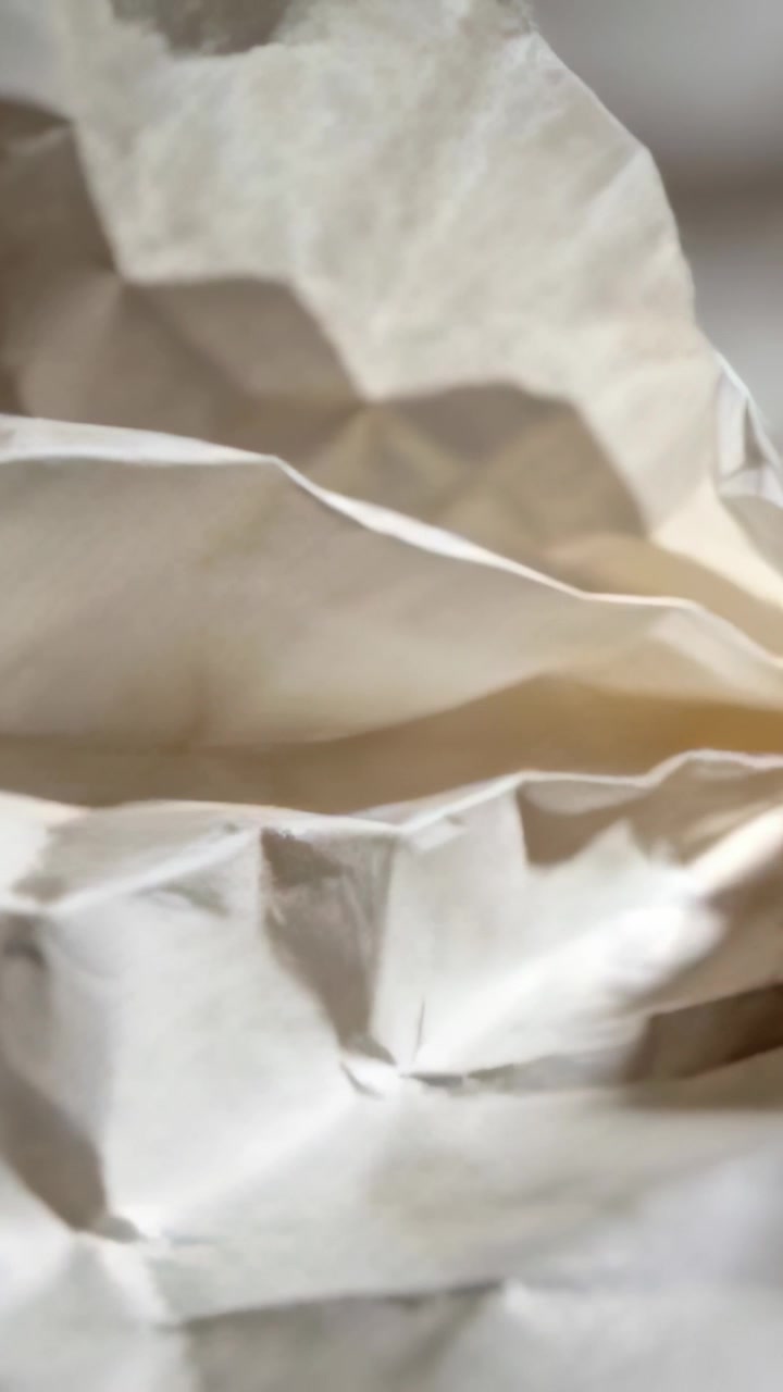 Video verticale: Telecamera che si sposta rivelando pieghe di carta leggera accartocciata in primo piano, mostrando la texture.