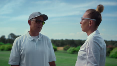 Couple-golf-players-talk-at-grass-course-field.-Golfers-team-chat-on-summer-day.