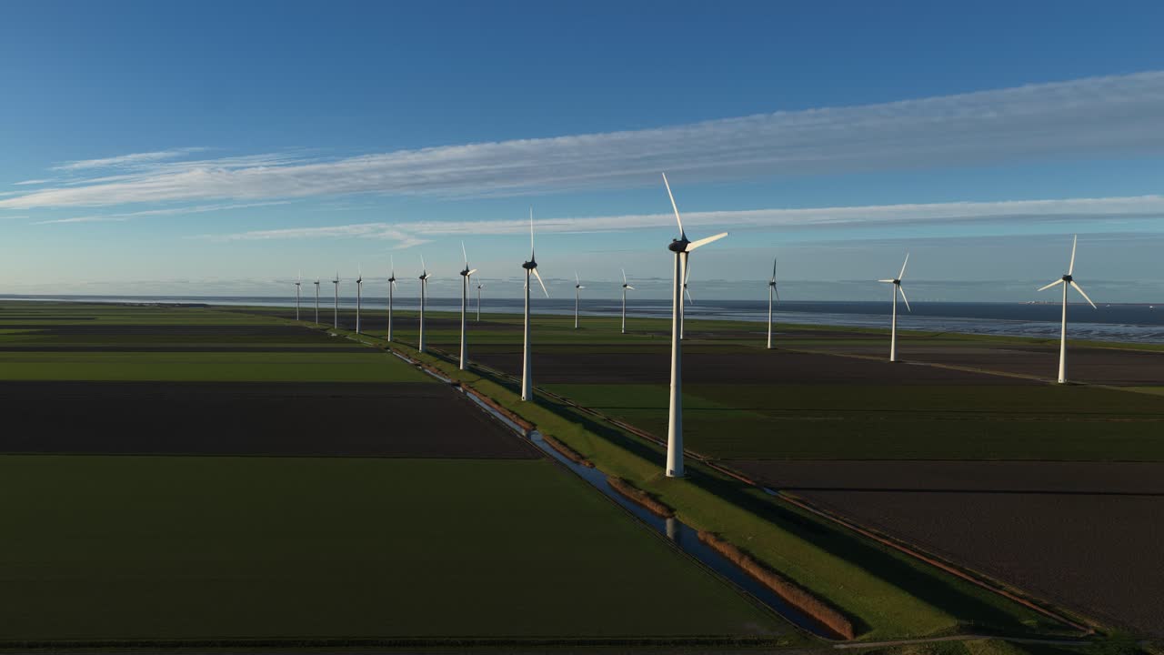 Aerial drone video of the large onshore wind farm in Eemshaven, Netherlands, showcasing numerous rotating turbines generating clean, renewable energy along the open coastal landscape