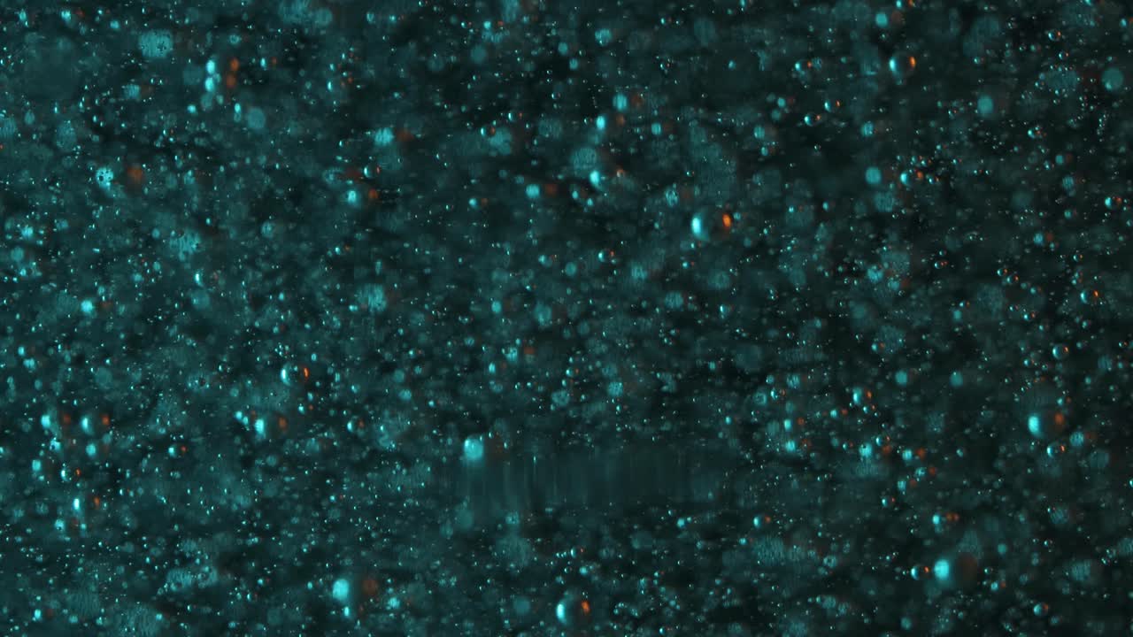 Bolle arancioni e verde acqua che salgono lentamente su uno sfondo scuro.