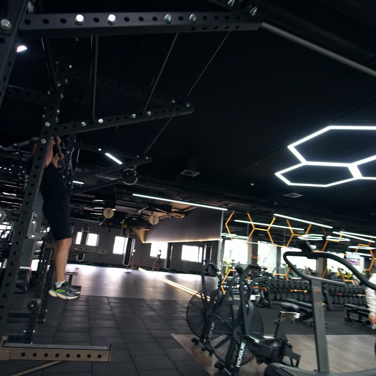 Confident muscular young man comes up to a horizontal bar and starts pulling up. Sportive lady doing squats with a horizontal bar on her shoulders