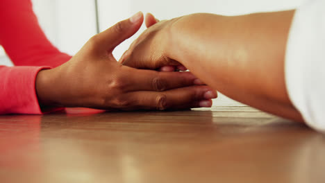 Mother-and-daughter-holding-hands-on-wooden-table-4k