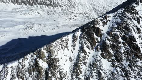 Luftaufnahme-Der-Bergwinterlandschaft-In-Großer-Höhe,-Schroffe-Steile-Hügel-Und-Schnee-An-Sonnigen-Tagen,-Filmische-Drohnenaufnahme