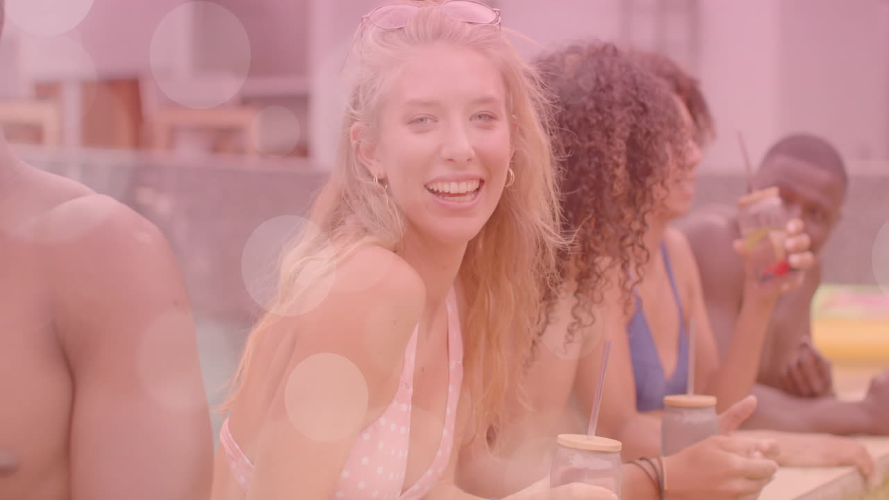 Smiling friends enjoying drinks by pool with bokeh light animation overlay