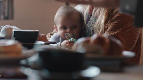 Madre-Joven-Cuidando-Al-Bebé-En-La-Cafetería-Usando-Chupete-Criando-A-Un-Niño-Relajándose-En-Un-Concurrido-Restaurante-Disfrutando-De-La-Maternidad