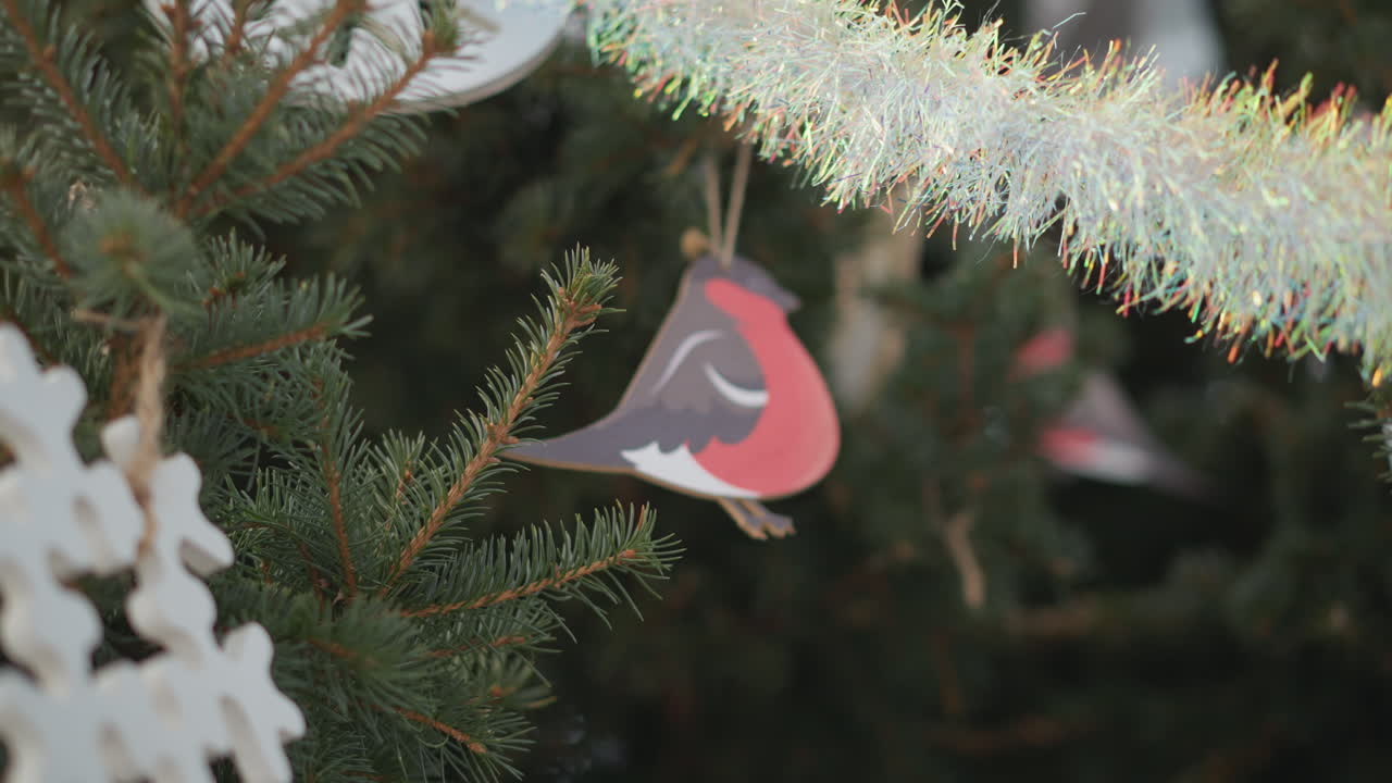 vista de cerca de un árbol festivo hermosamente decorado con un ornamento de pájaro tallado en madera que se balancea suavemente. las decoraciones de copos de nieve y las guarniciones relucientes mejoran el espíritu navideño