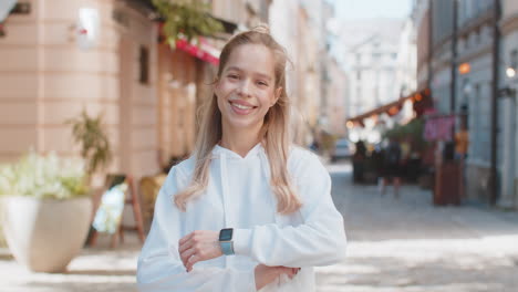 portrait of young caucasian woman tourist standing arms crossed looking at camera on city street